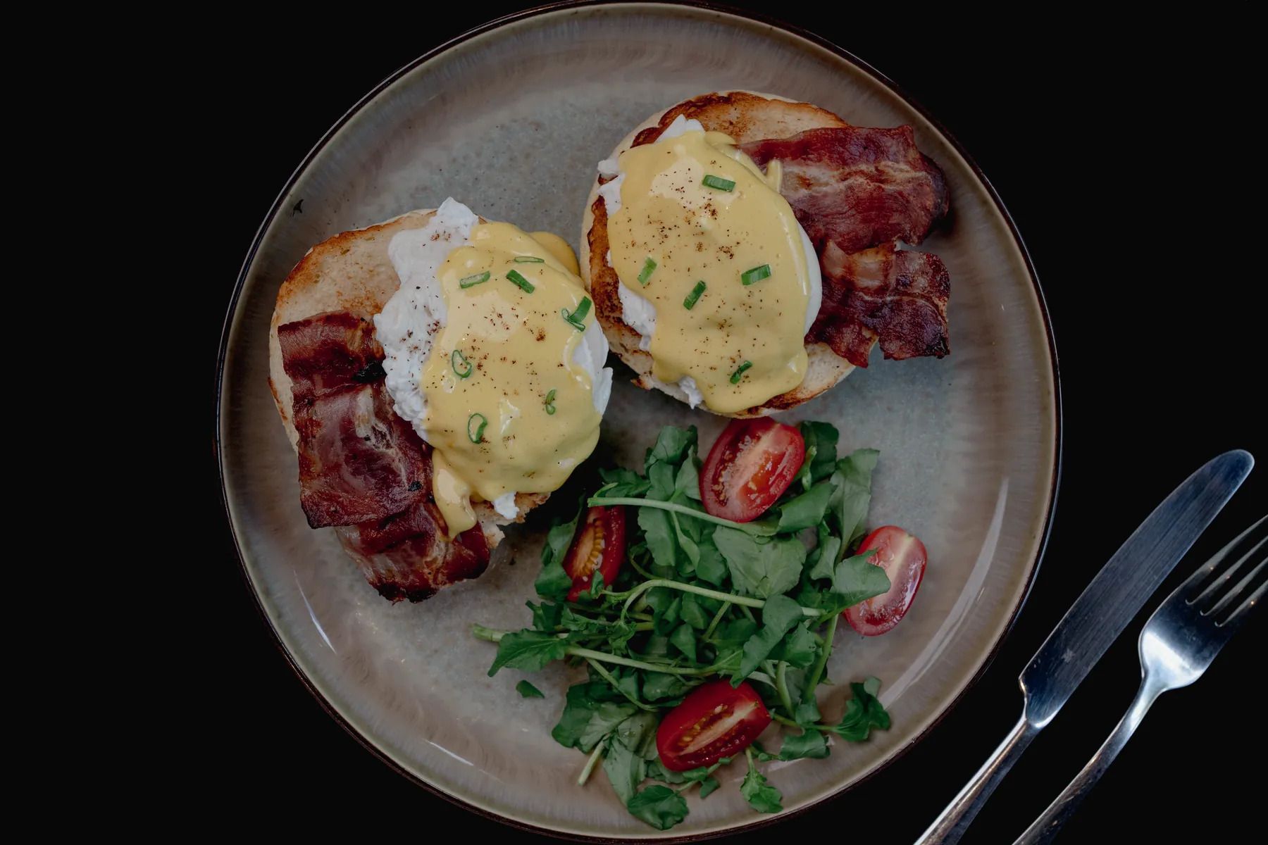 Eggs benedict dengan bacon, hollandaise, dan salad arugula