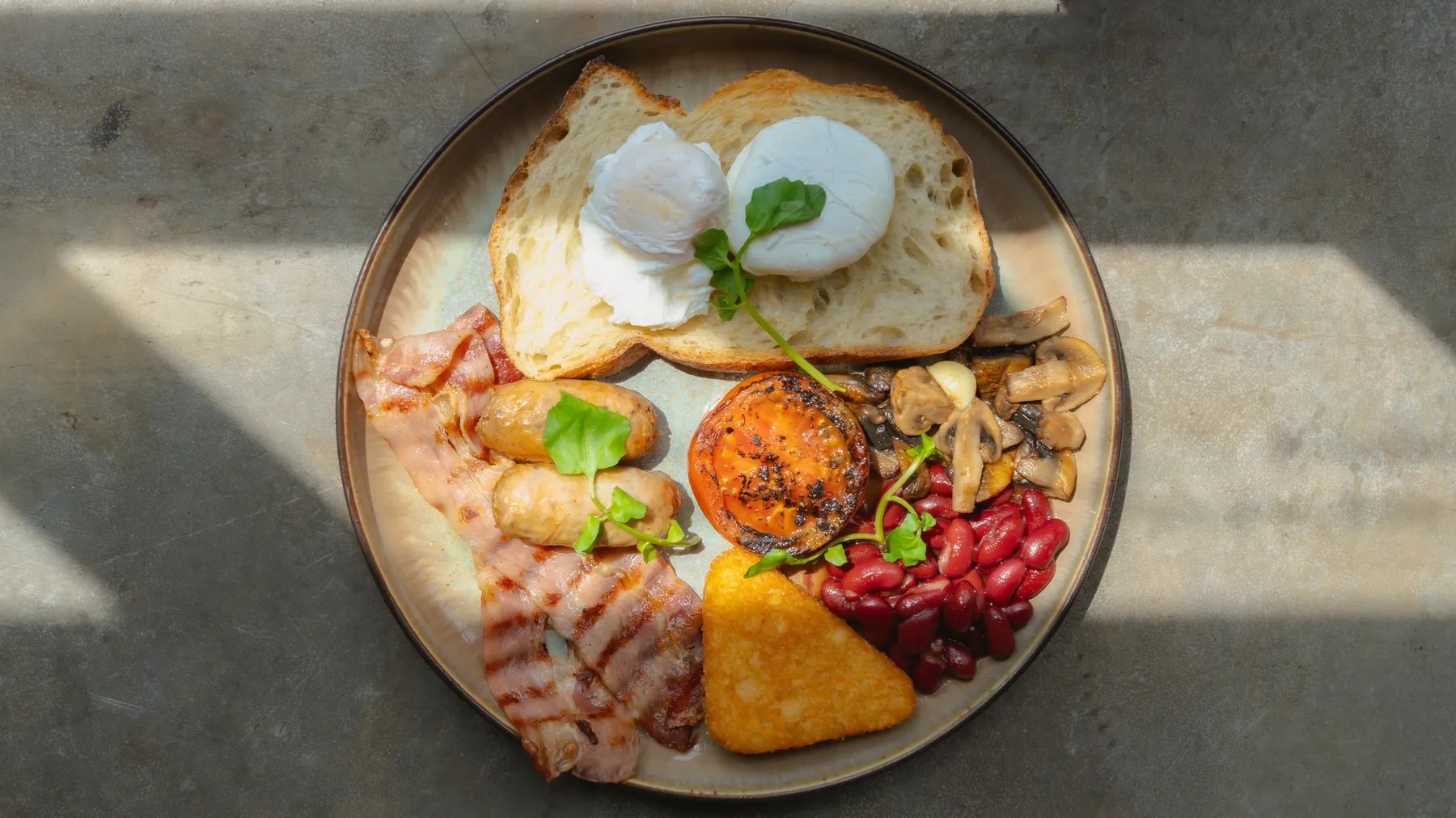 Full breakfast plate with poached eggs, bacon, and sourdough in morning sunlight