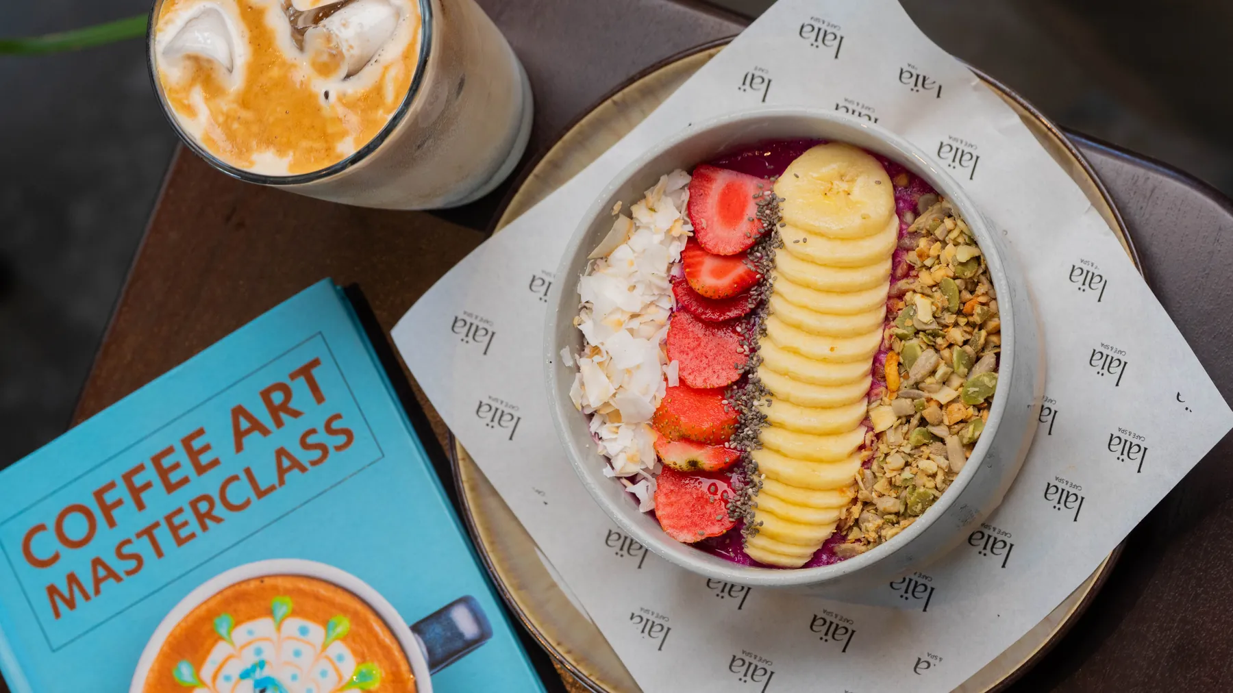 Dragon fruit smoothie bowl with banana, strawberry and granola, served beside an iced latte