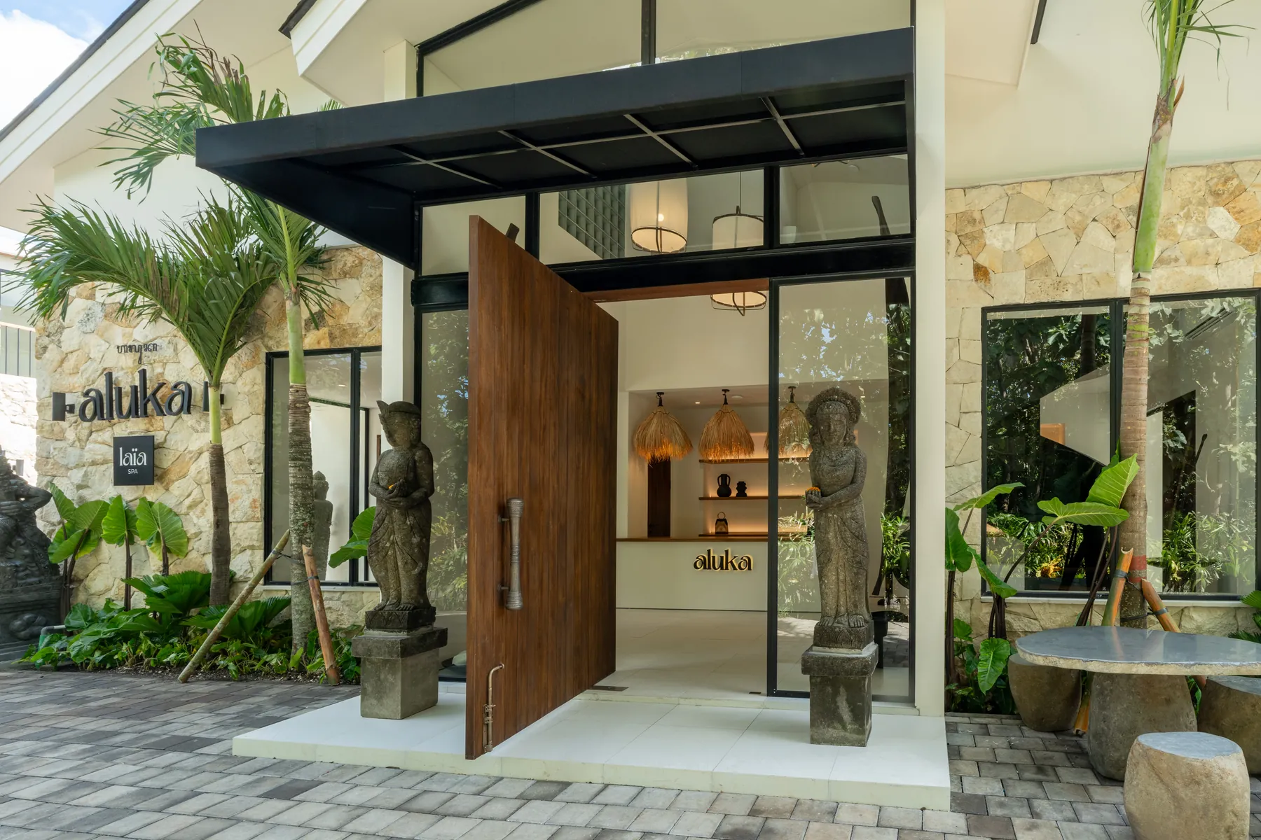 Aluka entrance with a tall wooden pivot door flanked by Balinese statues