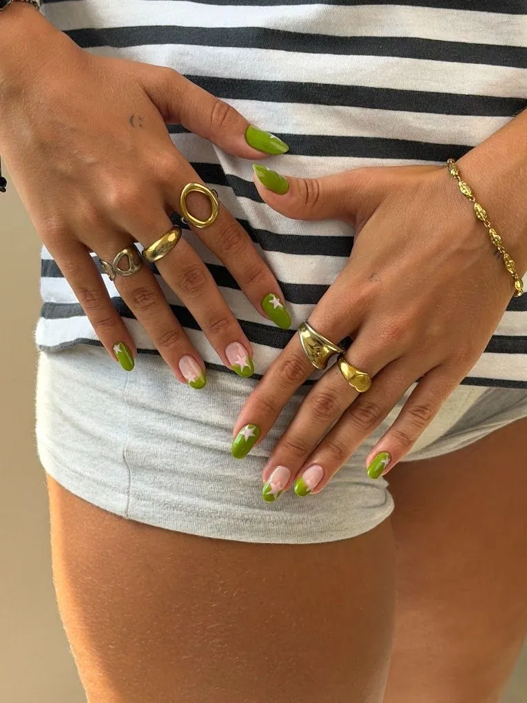 Olive green nails with white star accents and green French tips at Nāilu