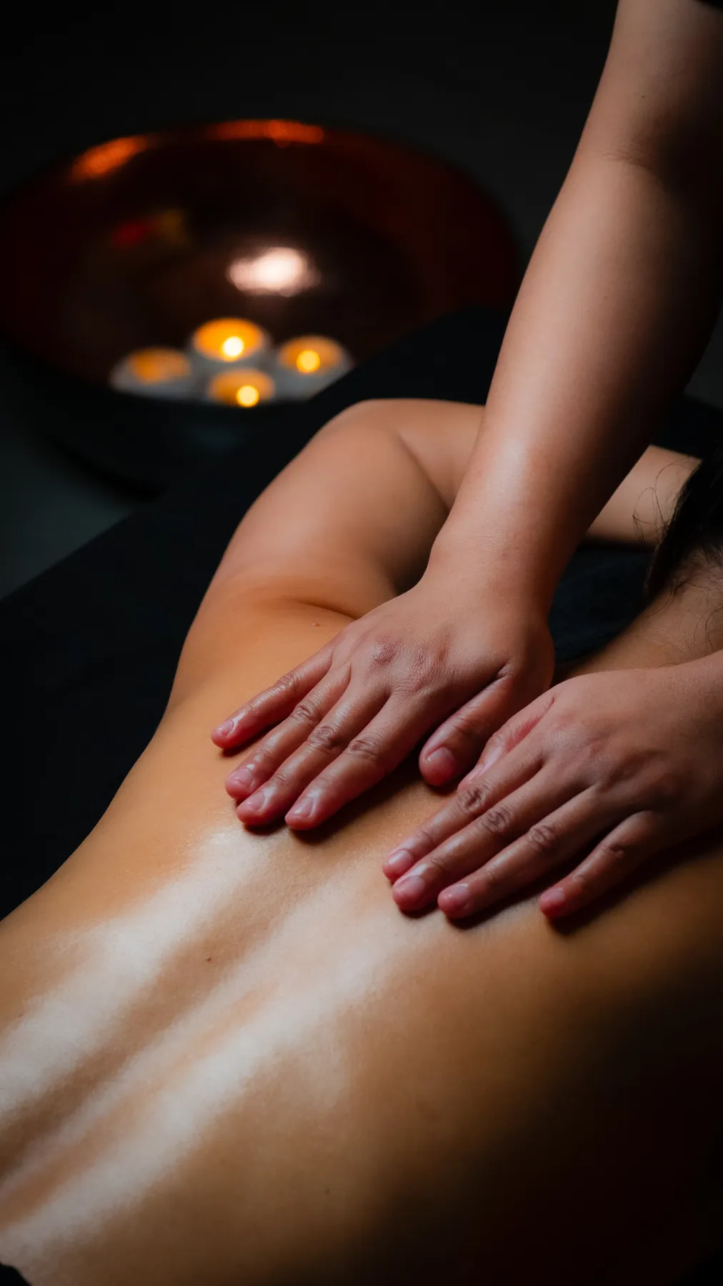 Back massage with warm oil beside a copper bowl of candles