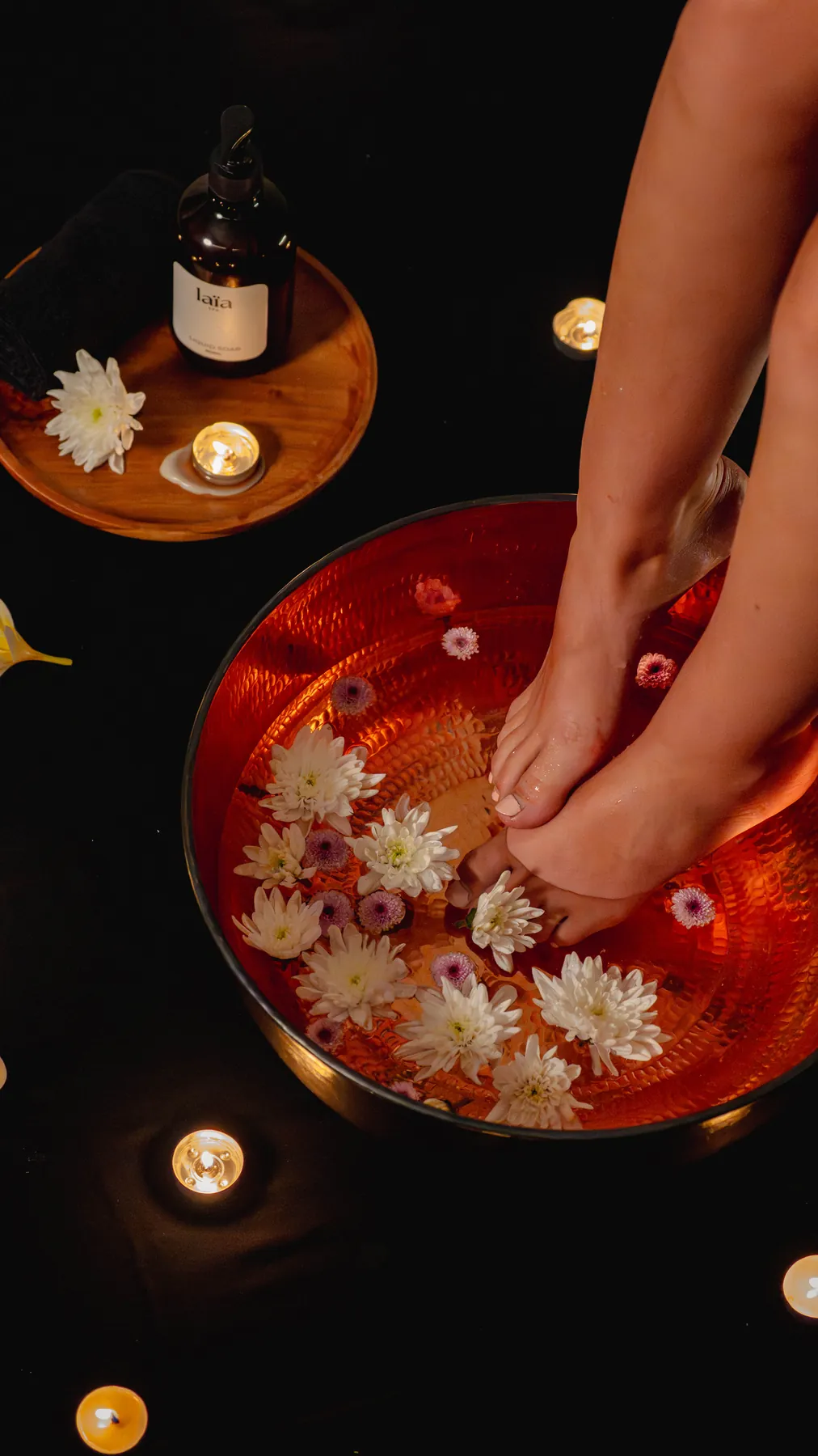 Rendaman kaki bertabur kelopak bunga dalam mangkuk tembaga di bawah cahaya lilin