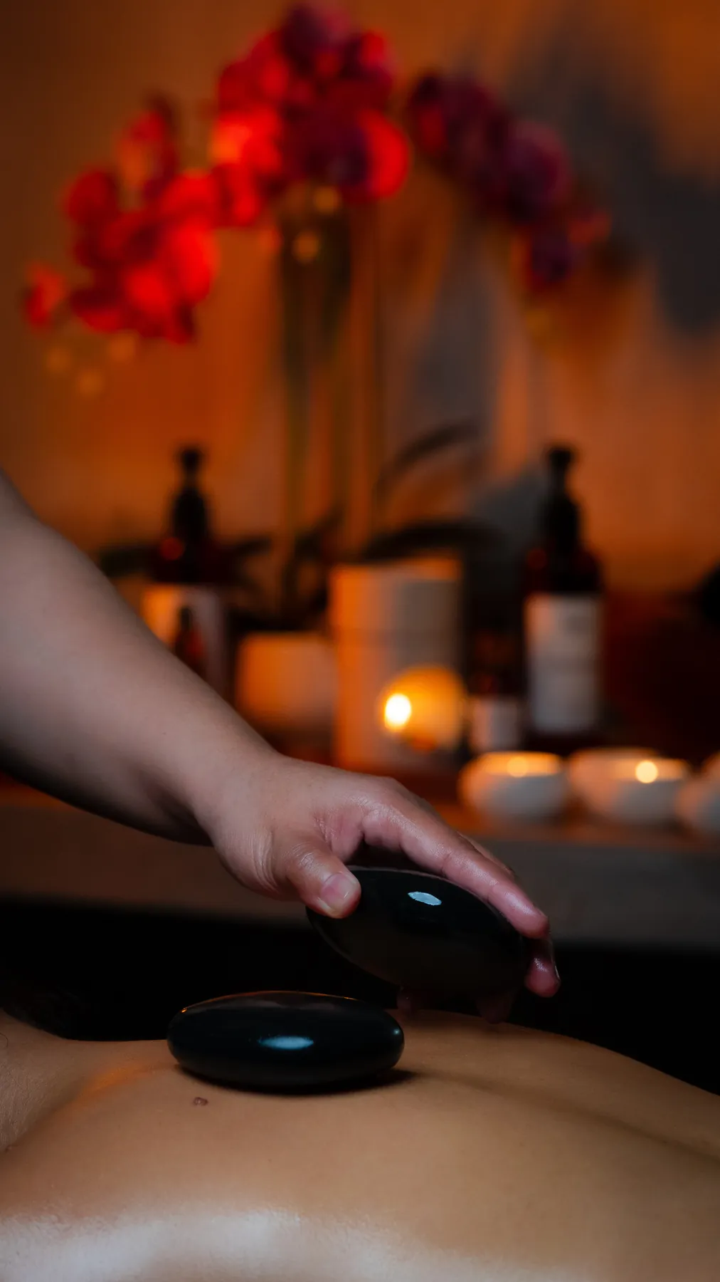 A hot stone massage by candlelight, with orchids and oils on the shelf behind